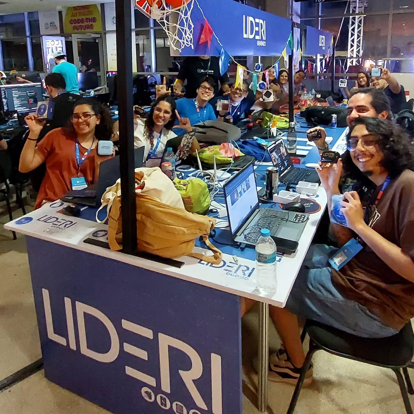 Estande LIDERI na Campus Party 2024 com participantes reunidos ao redor da bancada de tecnologia